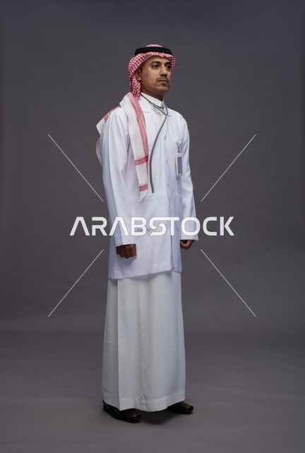 طبيب عربي سعودي خليجي يرتدي الثوب والمعطف الابيض مع سماعة الطب يقوم بايماءات واشارات مختلفه, كامل الجسم, خلفيه رماديه