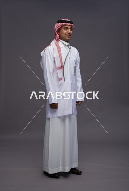 طبيب عربي سعودي خليجي يرتدي الثوب والمعطف الابيض مع سماعة الطب يقوم بايماءات واشارات مختلفه, كامل الجسم, خلفيه رماديه