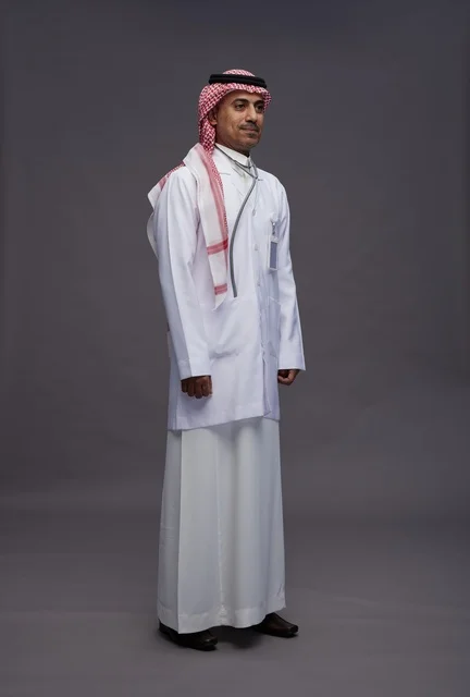 طبيب عربي سعودي خليجي يرتدي الثوب والمعطف الابيض مع سماعة الطب يقوم بايماءات واشارات مختلفه, كامل الجسم, خلفيه رماديه