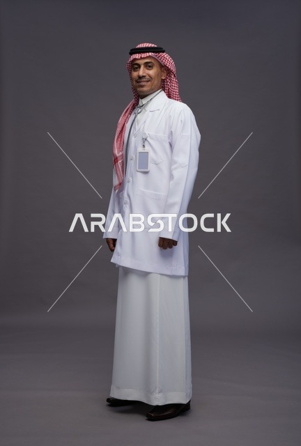 طبيب عربي سعودي خليجي يرتدي الثوب والمعطف الابيض مع سماعة الطب يقوم بايماءات واشارات مختلفه, كامل الجسم, خلفيه رماديه