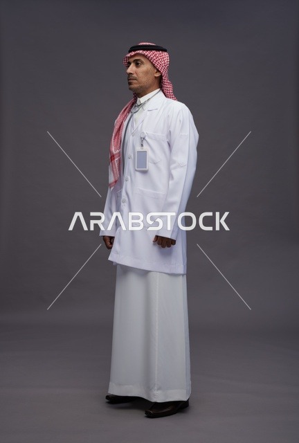 طبيب عربي سعودي خليجي يرتدي الثوب والمعطف الابيض مع سماعة الطب يقوم بايماءات واشارات مختلفه, كامل الجسم, خلفيه رماديه