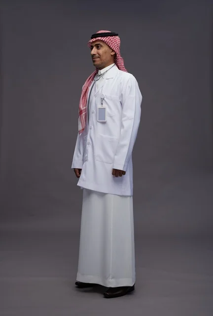 طبيب عربي سعودي خليجي يرتدي الثوب والمعطف الابيض مع سماعة الطب يقوم بايماءات واشارات مختلفه, كامل الجسم, خلفيه رماديه