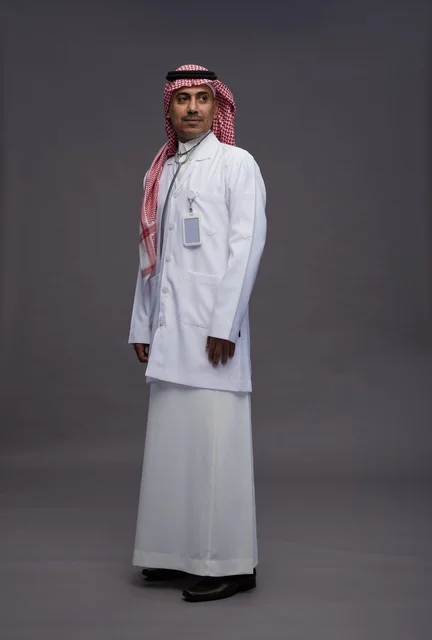 طبيب عربي سعودي خليجي يرتدي الثوب والمعطف الابيض مع سماعة الطب يقوم بايماءات واشارات مختلفه, كامل الجسم, خلفيه رماديه