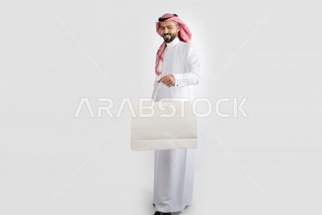 Portrait of a Saudi Arabian man carrying a white bag, a Saudi Gulf dress, with a white background