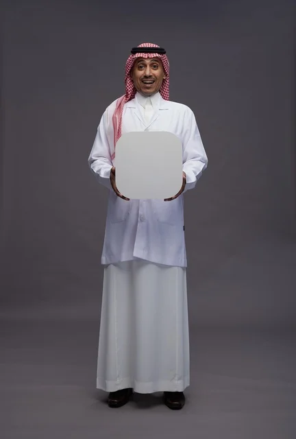 A portrait of an Arab Saudi Gulf doctor wearing a medical coat pointing to a blank white square board, a marketing advertisement board, full body, gray background.