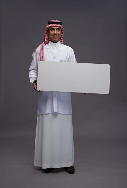 بورتريه لطبيب عربي سعودي  خليجي يرتدي المعطف الطبي يشير إلى لوح مربع ابيض فارغ , لوحه اعلانيه تسويقيه, كامل الجسم, خلفيه رماديه