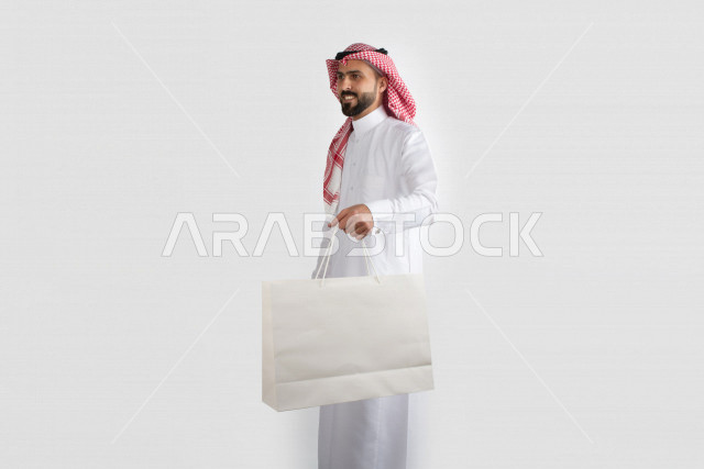 Portrait of a Saudi Arabian man carrying a white bag, a Saudi Gulf dress, with a white background