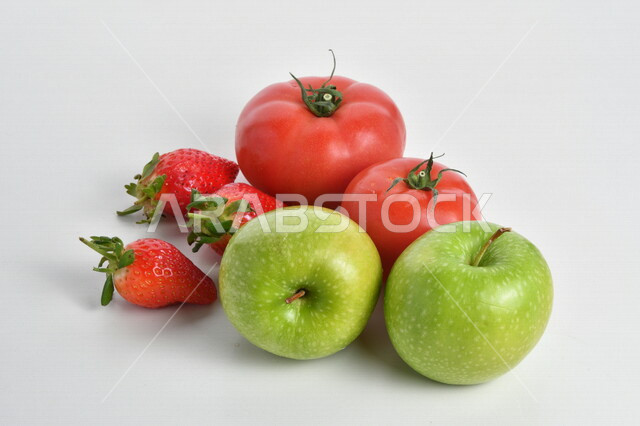 صورة مقربة لفاكهة التفاح الأخضر والطماطم الحمراء والفراولة اللذيذة مصورة على خلفية بيضاء ، الخضراوات والفواكة الطازجة المفيدة للصحة ، فطور يومي ، حمية غذائية صحية