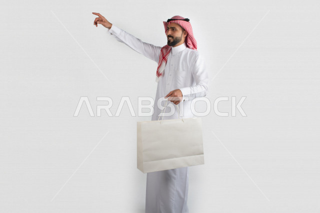 Portrait of a Saudi Arabian man carrying a white bag, a Saudi Gulf dress, with a white background