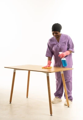 عاملة نظافة أفريقية تنظف طاولة خشبية بزي أرجواني