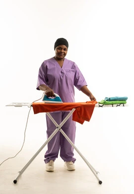 African Female Worker Ironing Clothes in Purple Uniform
