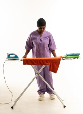 امرأة أفريقية بزي العمل الأرجواني تكوي الملابس