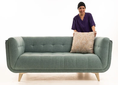 امرأة بزي العمل تضع وسادة على أريكة خضراء