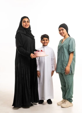 امرأة سعودية مع طفل وعاملة منزلية يحملون كعكة