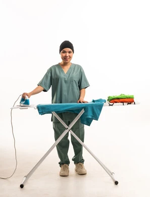 East Asian Housekeeper Ironing Clothes in Green Scrubs