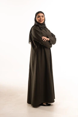 امرأة سعودية بعباءة داكنة تقف مبتسمة ومكتوفة اليدين