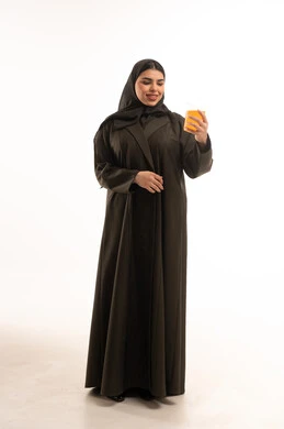 امرأة سعودية بالعباءة تحمل كوب عصير برتقال