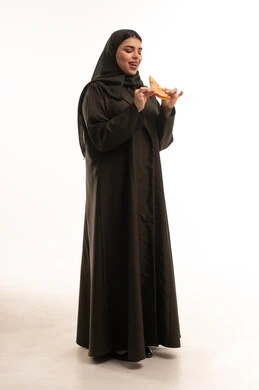 امرأة سعودية بالعباءة تأكل البيتزا أمام خلفية بيضاء