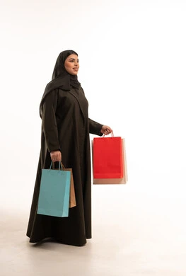 امرأة سعودية بالعباءة السوداء تحمل أكياس تسوق