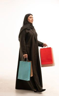امرأة سعودية بالعباءة تمشي مع حقائب تسوق ملونة