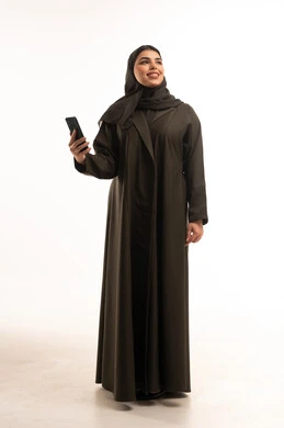 امرأة سعودية بالعباءة تحمل هاتفاً ذكياً في الاستوديو