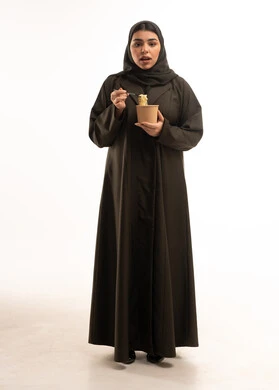 امرأة عربية بالعباءة السوداء تحمل علبة طعام