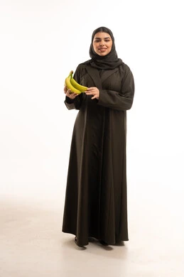 امرأة سعودية بالعباءة تمسك موز أخضر