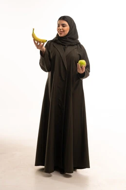 امرأة سعودية بالعباءة تحمل موزة وتفاحة خضراء