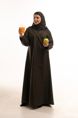 امرأة سعودية تحمل عصير برتقال وتفاحة خضراء