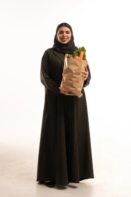 امرأة إماراتية بالعباءة تحمل حقيبة خضروات طازجة