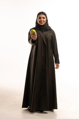 امرأة سعودية بالعباءة تحمل تفاحة خضراء في الاستوديو