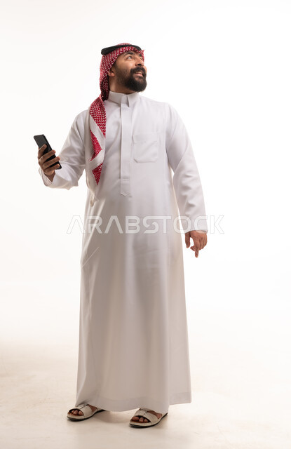 رجل سعودي بالزي التقليدي يمسك هاتفاً ذكياً