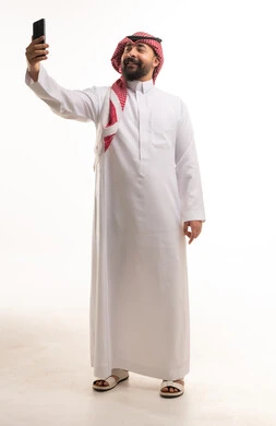 رجل سعودي بالزي التقليدي يلتقط صورة سيلفي بالجوال