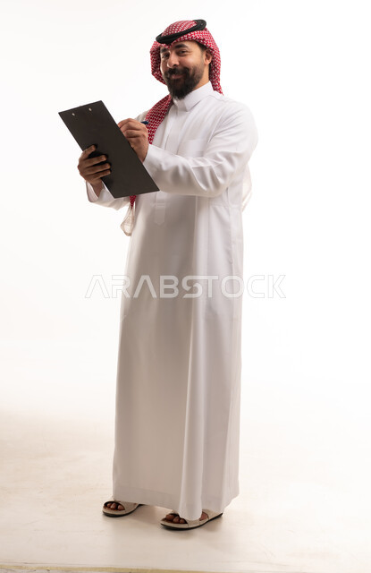 رجل سعودي يرتدي الثوب التقليدي ويكتب على ملف في الاستوديو
