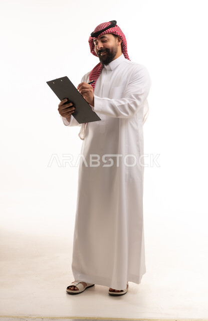رجل سعودي بالزي التقليدي يكتب على لوحة ملاحظات بيضاء
