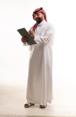 رجل سعودي بالزي التقليدي يكتب على لوحة ملاحظات بيضاء