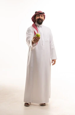 رجل سعودي بالزي التقليدي يحمل تفاحة خضراء