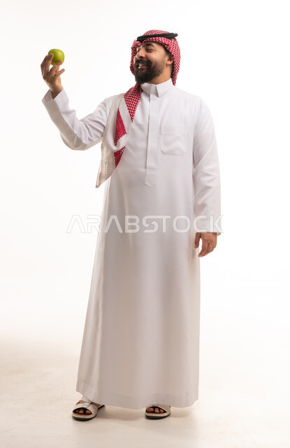 رجل سعودي بالزي التقليدي يحمل تفاحة خضراء