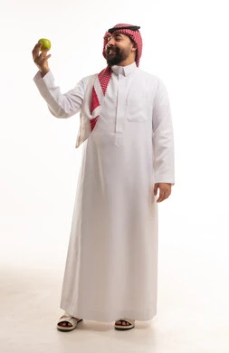 رجل سعودي بالزي التقليدي يحمل تفاحة خضراء