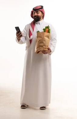 رجل سعودي يحمل كيس خضروات وهاتف ذكي