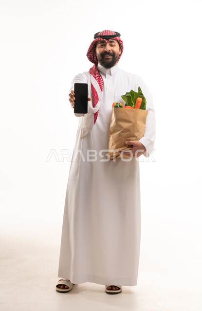 رجل سعودي يحمل كيس خضروات وهاتف ذكي