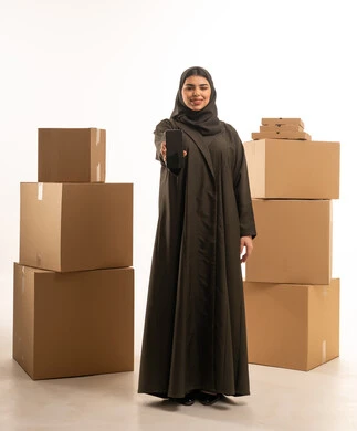 امرأة سعودية تحمل هاتفاً ذكياً وصناديق شحن