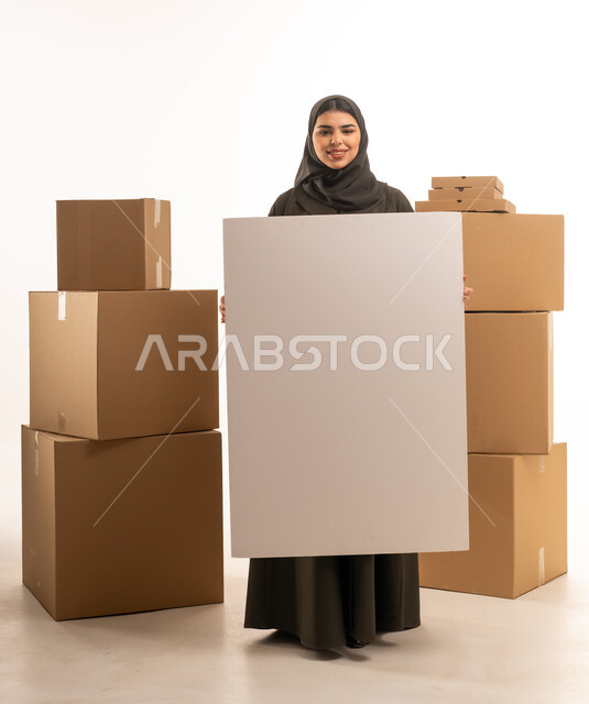 امرأة سعودية تحمل لوحة فارغة بجانب صناديق شحن
