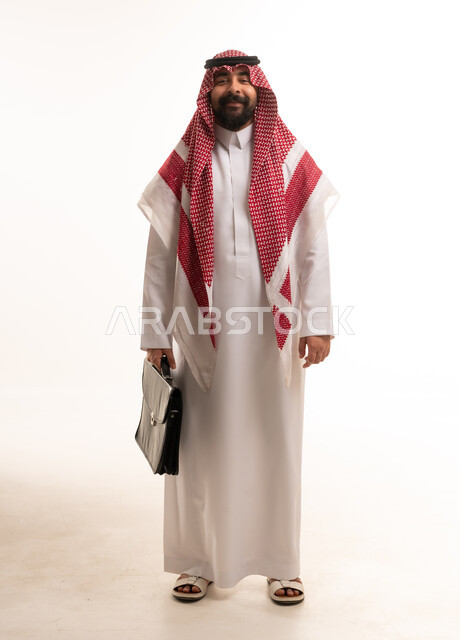 رجل أعمال سعودي بالثوب يحمل حقيبة عمل في الاستوديو