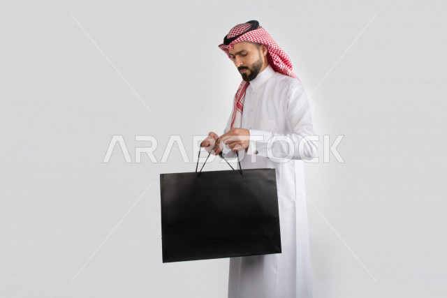 بورتريه رجل سعودي عربي يحمل حقيبة باللون الأسود ، بلباس السعودية التقليدية , بخلفية بيضاء