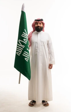 رجل سعودي يمسك بالعلم الوطني على خلفية بيضاء