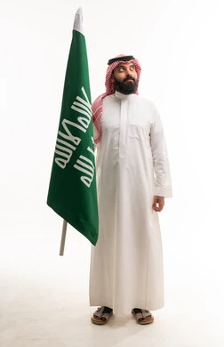 رجل سعودي بالزي التقليدي يحمل علم المملكة