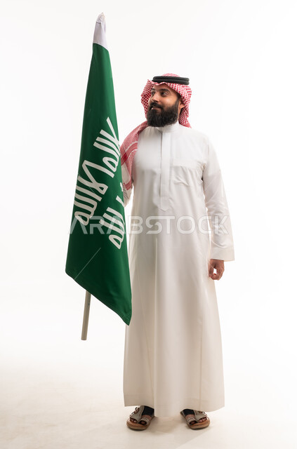 رجل سعودي بالزي التقليدي يحمل علم السعودية
