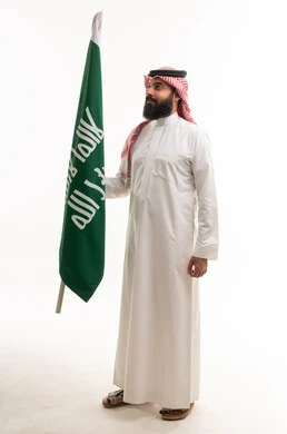 رجل سعودي بالزي التقليدي يحمل علم المملكة العربية السعودية