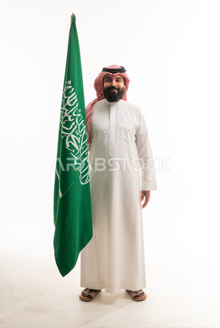 رجل سعودي بالزي التقليدي مع العلم الوطني